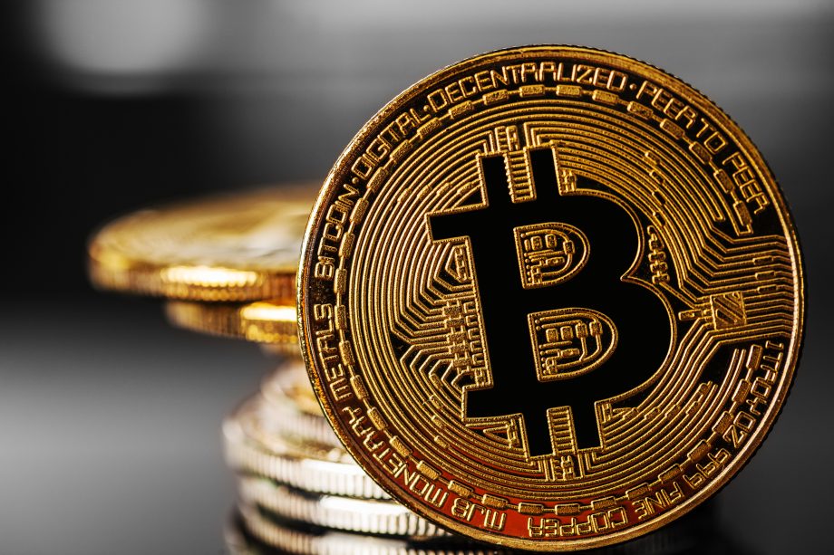 Nahaufnahme einer physischen Bitcoin-Münze mit dem Bitcoin-Logo, gestapelt auf anderen Münzen, die den wachsenden Einfluss von Bitcoin in der Welt der digitalen Kryptowährungen symbolisieren.