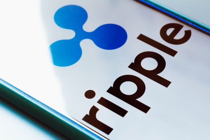 Auf einem Smartphone-Bildschirm werden das Ripple-Stablecoin-Logo und der Name in fetten schwarzen Buchstaben angezeigt, wobei das RLUSD-Logo in Blau über dem Text erscheint.