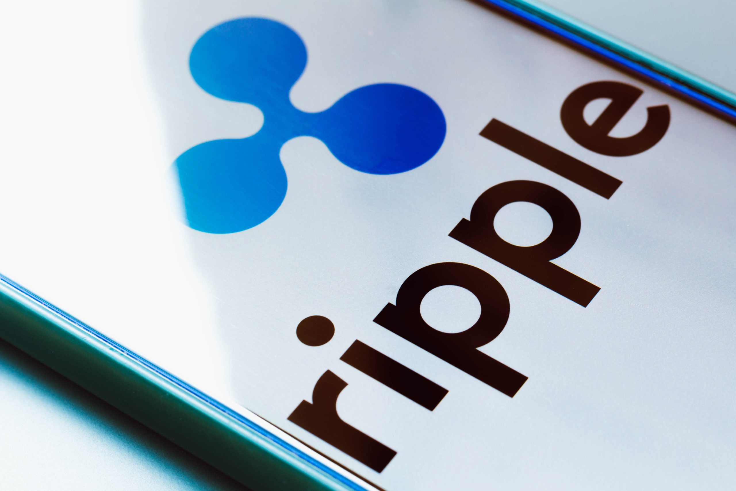 Auf einem Smartphone-Bildschirm werden das Ripple-Stablecoin-Logo und der Name in fetten schwarzen Buchstaben angezeigt, wobei das RLUSD-Logo in Blau über dem Text erscheint.