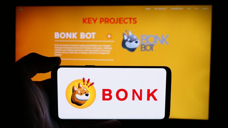 Ein Smartphone zeigt das BONK-Logo vor einem Bildschirm mit spannenden BONK Bot-Projektdetails, alles vor einem leuchtend gelben Hintergrund.