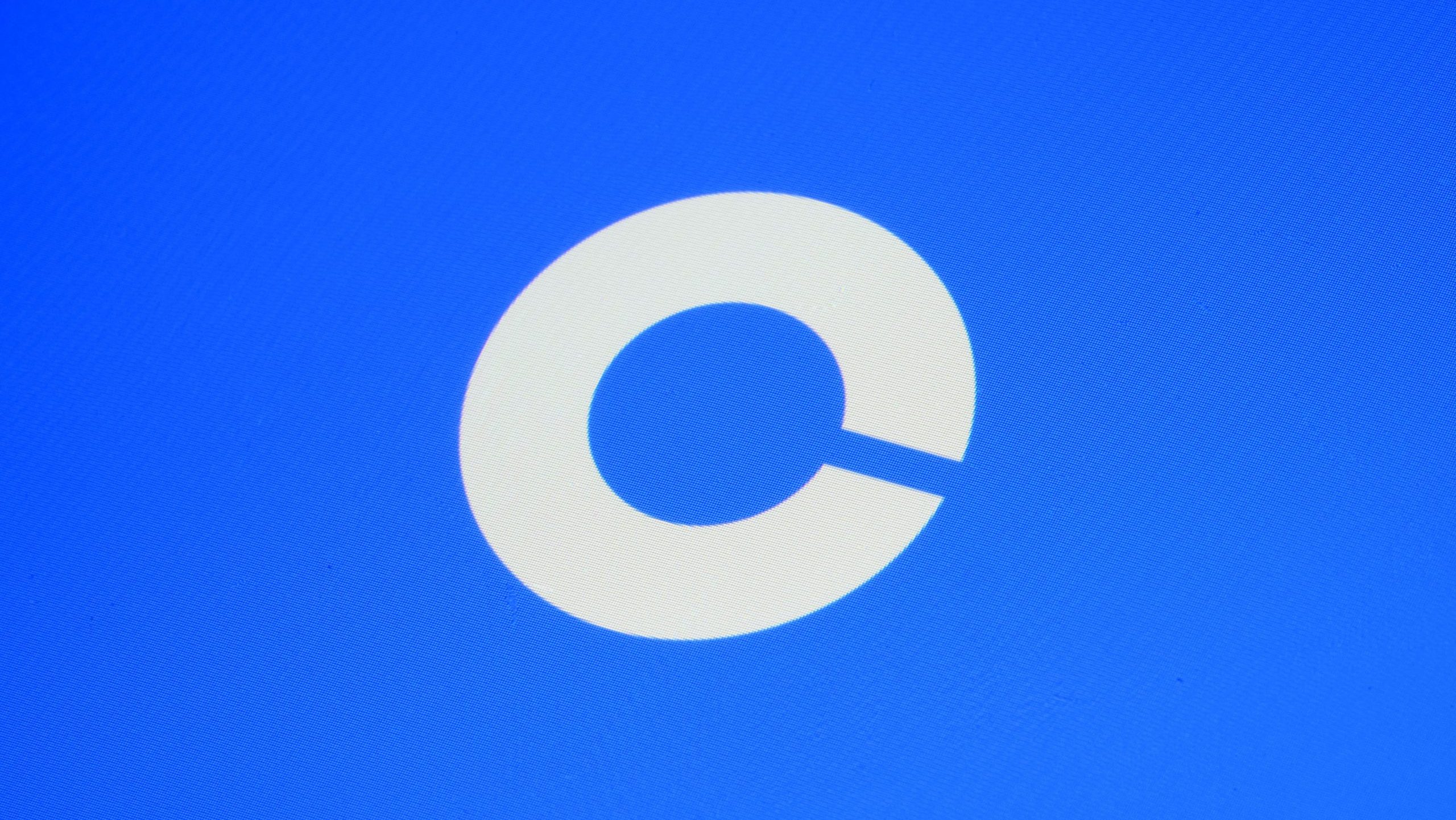 Ein weißes, kreisförmiges Coinbase-Logo mit einer kleinen Lücke unten rechts auf blauem Hintergrund.