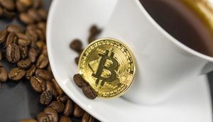 Eine goldene Bitcoin-Münze ruht auf einer weißen Kaffeetasse, die mit Kaffee gefüllt und von verstreuten Kaffeebohnen umgeben ist - eine stilvolle Anspielung auf die Welt der Kryptowährung.