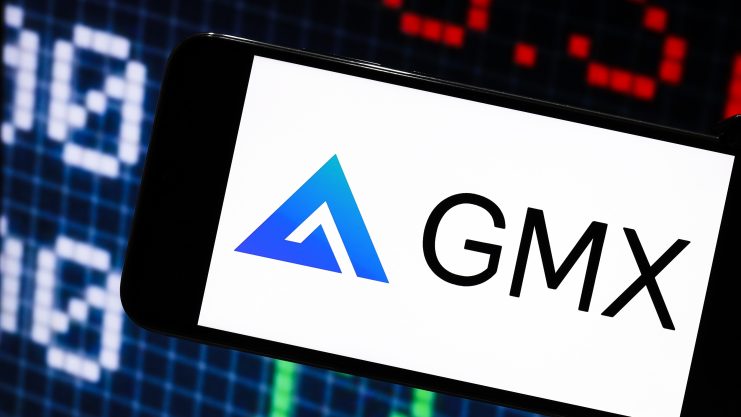 Ein Smartphone zeigt das GMX-Logo und den Namen vor einem digitalen Börsenbildschirm mit blauen und roten Tickerdaten, die die Trends auf den Kryptomärkten hervorheben.