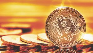 Eine Nahaufnahme einer Bitcoin-Münze, die aufrecht steht, mit anderen Münzen, die flach im Hintergrund liegen, alle in einen goldenen Farbton getaucht.
