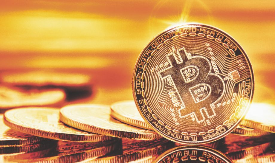Eine Nahaufnahme einer Bitcoin-Münze, die aufrecht steht, mit anderen Münzen, die flach im Hintergrund liegen, alle in einen goldenen Farbton getaucht.