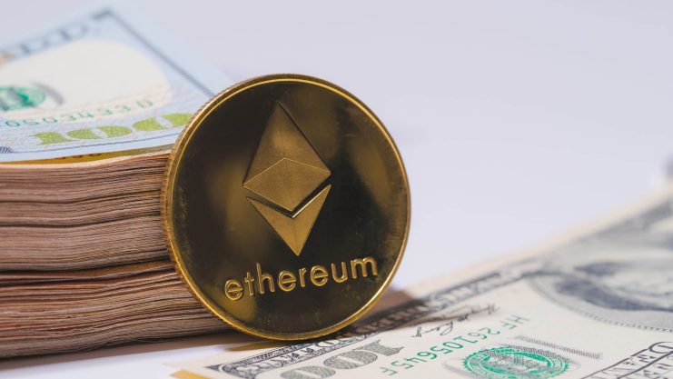 Eine goldene Ethereum-Münze steht aufrecht neben einem Stapel US-amerikanischer Hundert-Dollar-Scheine und einem einzelnen Hundert-Dollar-Schein auf einer weißen Fläche und hebt den Wert von Ethereum neben der traditionellen Währung hervor.
