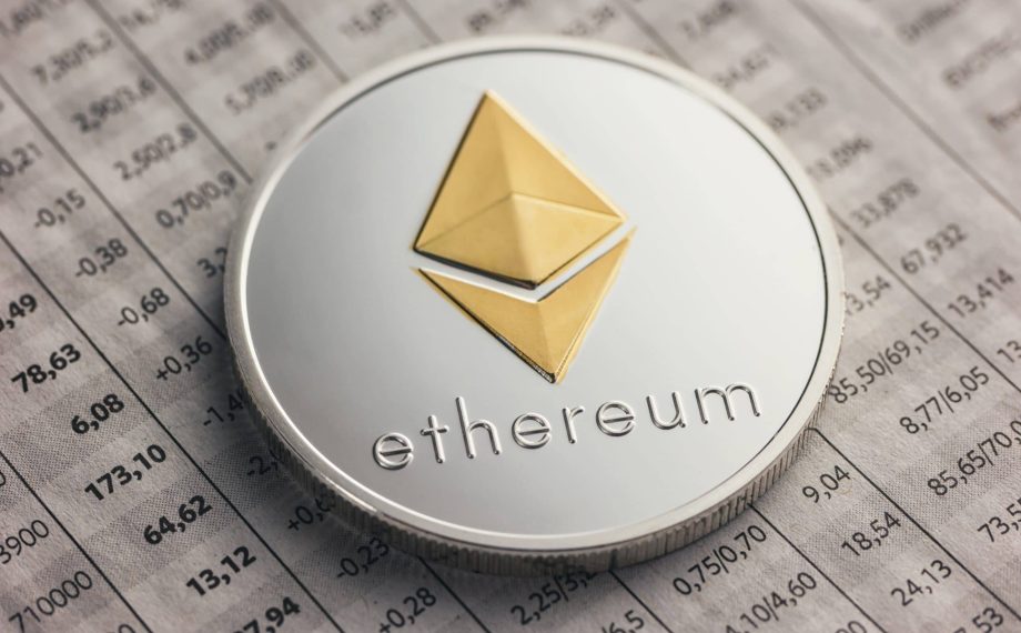 Eine physische Ethereum-Münze mit dem Ethereum-Logo und dem Wort ruht auf einer mit Zahlen gefüllten Finanztabelle.
