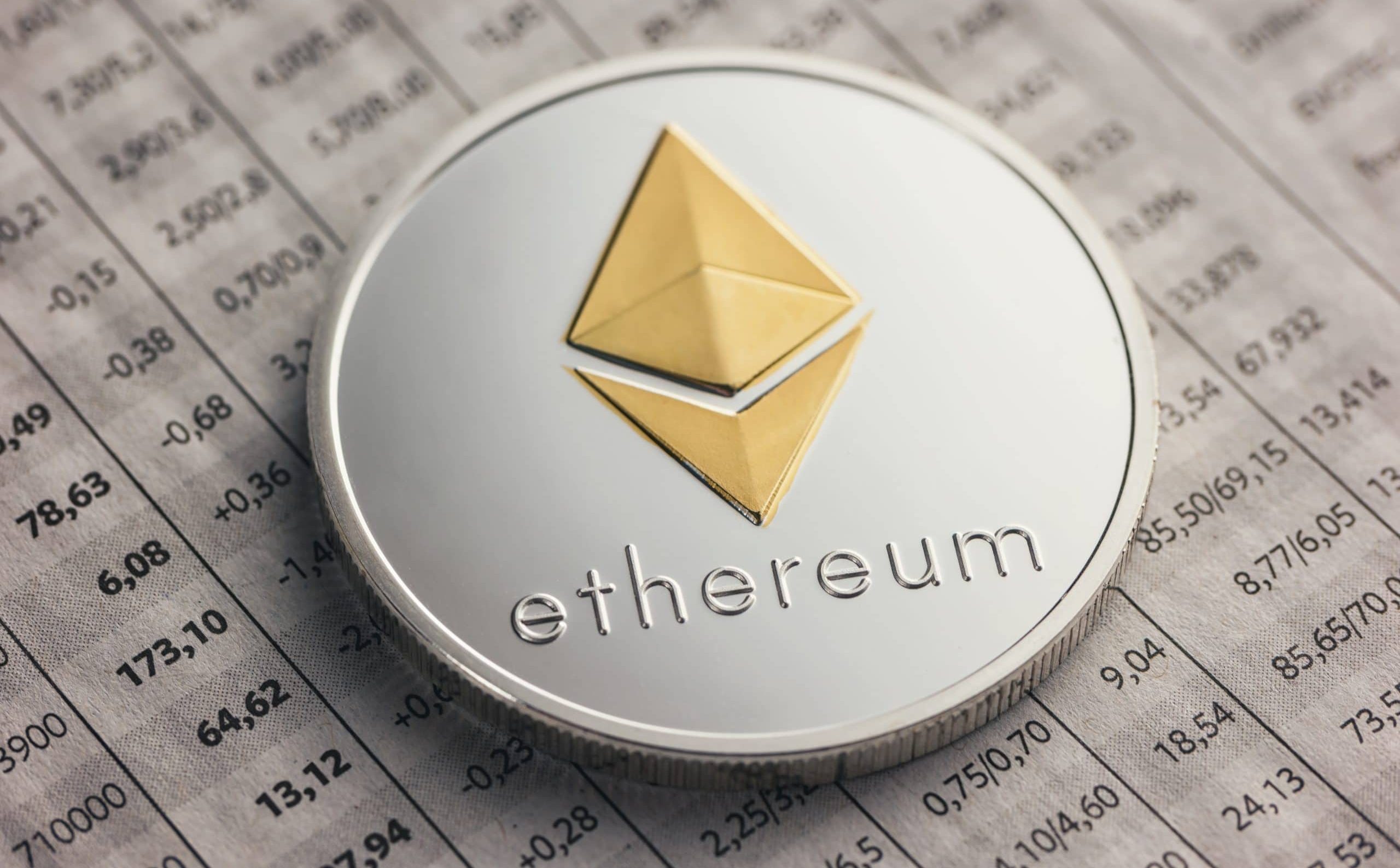 Eine physische Ethereum-Münze mit dem Ethereum-Logo und dem Wort ruht auf einer mit Zahlen gefüllten Finanztabelle.