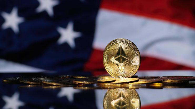 Eine goldene Ethereum-Münze steht aufrecht zwischen anderen Münzen, mit einer verschwommenen amerikanischen Flagge im Hintergrund, die den wachsenden Einfluss von Ethereum in der digitalen Währungslandschaft unterstreicht.