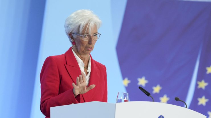Eine Frau in einem roten Blazer spricht an einem Podium mit der Aufschrift EZB-Europäische Zentralbank, im Hintergrund ist eine EU-Flagge zu sehen.