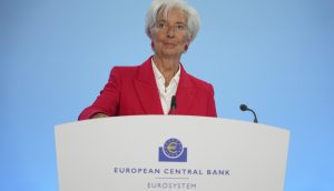 Eine Frau in einem roten Blazer steht an einem Podium mit der Aufschrift EZB Europäische Zentralbank Eurosystem und spricht vor einem blauen Hintergrund.