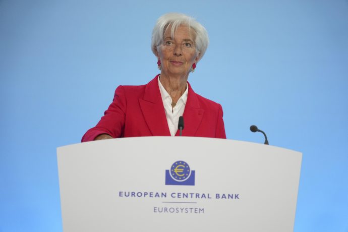 Eine Frau in einem roten Blazer steht an einem Podium mit der Aufschrift EZB Europäische Zentralbank Eurosystem und spricht vor einem blauen Hintergrund.