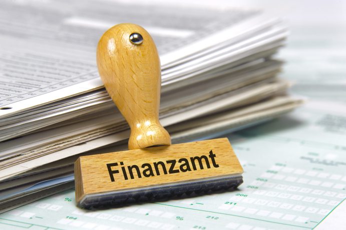 Ein hölzerner Stempel mit der Aufschrift Finanzamt prangt auf Papieren und Dokumenten und verweist auf das deutsche Finanzamt und die Krypto-Steuer-Vorschriften.
