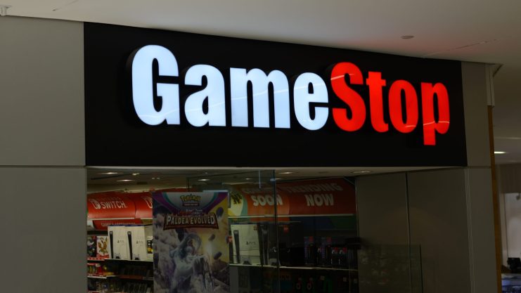 Das Äußere einer GameStop-Filiale mit einem schwarzen Schild, auf dem der Name des Geschäfts in weißer und roter Schrift über dem Eingang zu lesen ist, spiegelt die Präsenz von GameStop inmitten von Diskussionen über Bitcoin und Inflationsschutz wider.