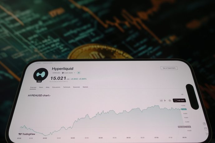 Auf einem Smartphone-Bildschirm wird ein Hyperliquid-Handelsdiagramm mit steigendem Wert angezeigt, während im Hintergrund eine unscharfe Bitcoin-Grafik und ein Finanzdiagramm die Marktaktivitäten von Hyperliquid hervorheben.