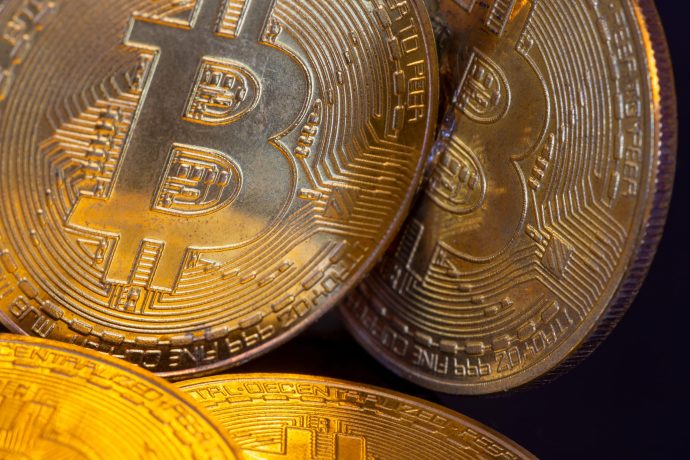 Nahaufnahme von drei physischen Münzen mit dem Bitcoin-Logo und kreislaufähnlichen Mustern, die das Wesen von Bitcoin und seine Rolle in der Kryptowährung hervorheben.