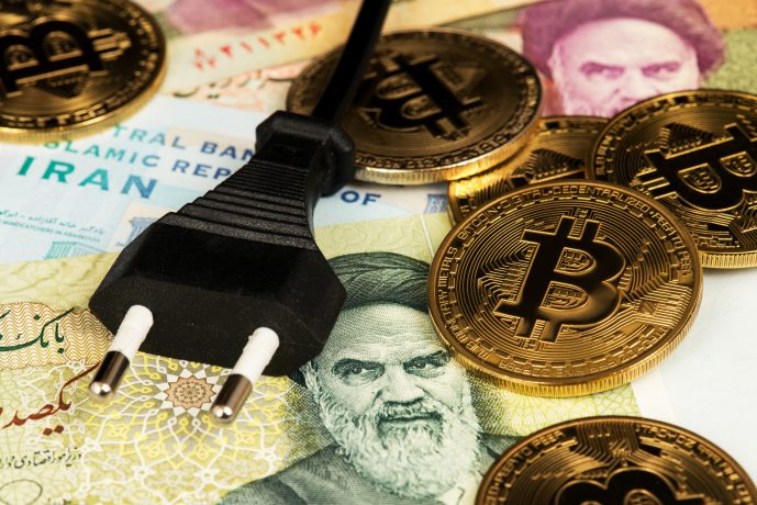 Ein schwarzer Stromstecker und mehrere goldene Bitcoin-Münzen liegen auf iranischen Banknoten mit Gesichtern, persischer Schrift und eindeutigen Symbolen des Iran.