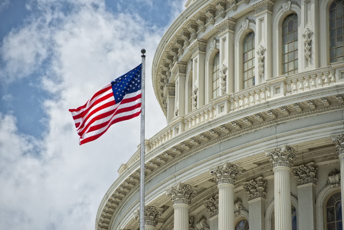 Vor der weißen Säulenfassade des Kapitols der Vereinigten Staaten weht bei teilweise bewölktem Himmel eine amerikanische Flagge, ein Symbol für aktuelle Debatten wie die Krypto-Gesetzesblockade in der Finanzpolitik.