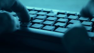 Nahaufnahme von Händen, die auf einer Computertastatur in einem blauen Farbton tippen, der an die schnelllebige Welt von Krypto erinnert.
