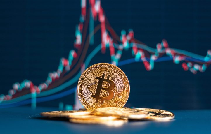 Eine Bitcoin-Münze steht aufrecht zwischen anderen Münzen, mit einem bunten Krypto-Kursdiagramm im verschwommenen Hintergrund.