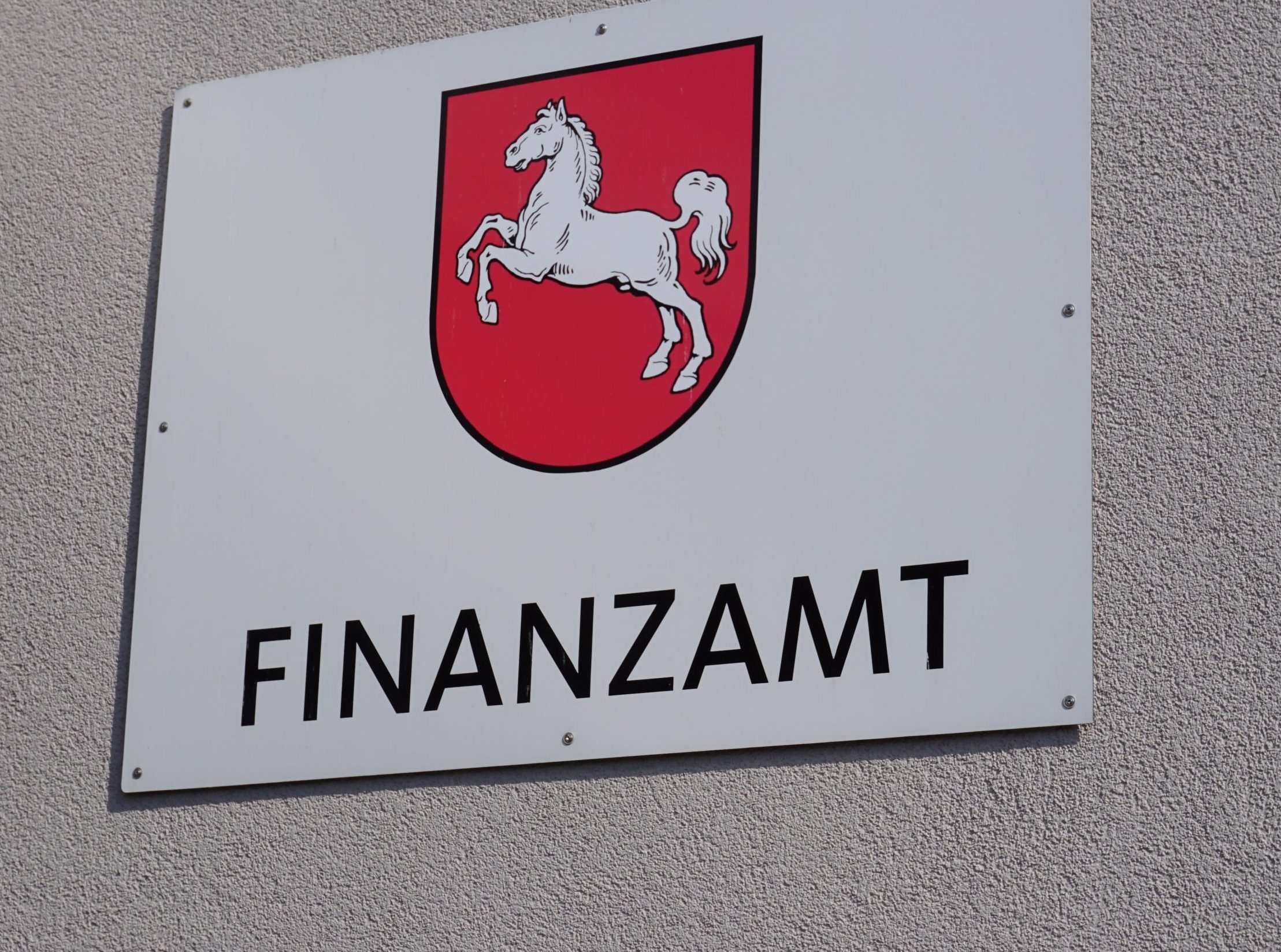 Ein Schild an der Wand zeigt ein rotes Schild mit einem weißen Pferd und dem Wort Finanzamt darunter, was auf die Rolle des Amtes bei der Überwachung der Krypto-Steuern hinweist.