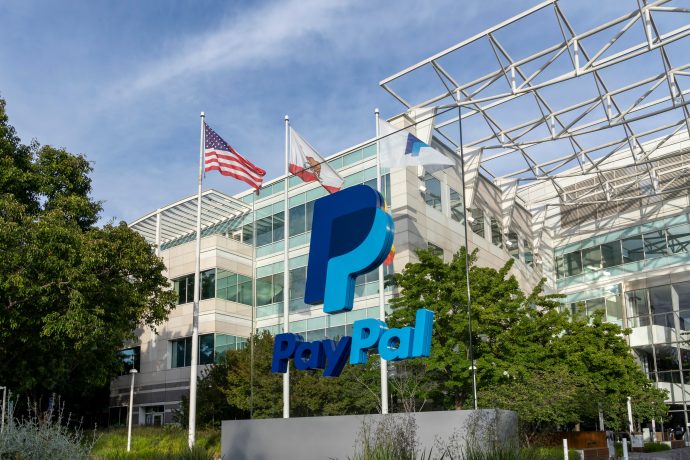 PayPal-Hauptquartier mit großem PayPal-Logo vor dem Gebäude, umgeben von Bäumen und mehreren Flaggen, darunter die amerikanische Flagge, die die Rolle von PayPal im Bitcoin-Ökosystem inmitten der jüngsten Aktienrallye hervorhebt.