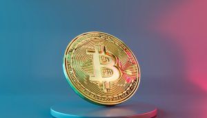 Eine goldene Bitcoin-Münze steht aufrecht auf einem runden Podest, ihre glänzende Oberfläche fängt das Licht vor einem Hintergrund mit blauem und rosa Farbverlauf ein.
