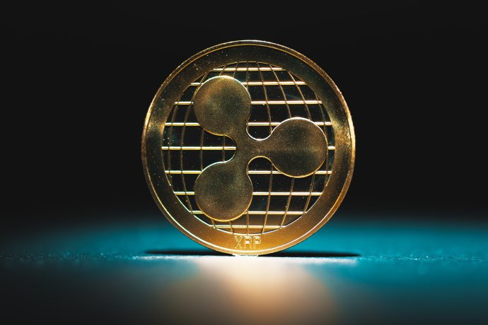 Eine goldene XRP-Kryptowährungsmünze steht aufrecht auf einer dunklen, von blauem Licht beleuchteten Fläche.