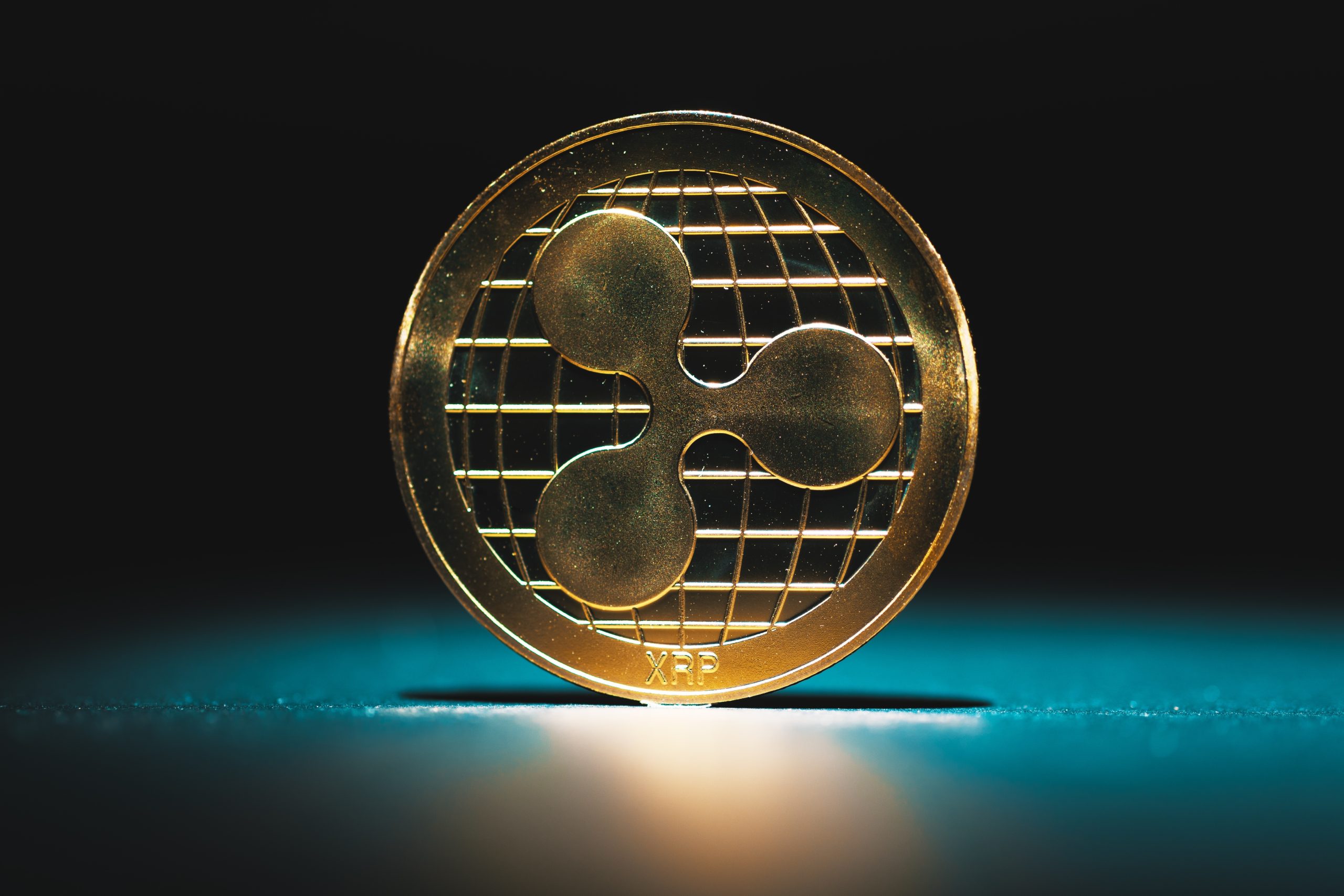 Eine goldene XRP-Kryptowährungsmünze steht aufrecht auf einer dunklen, von blauem Licht beleuchteten Fläche.