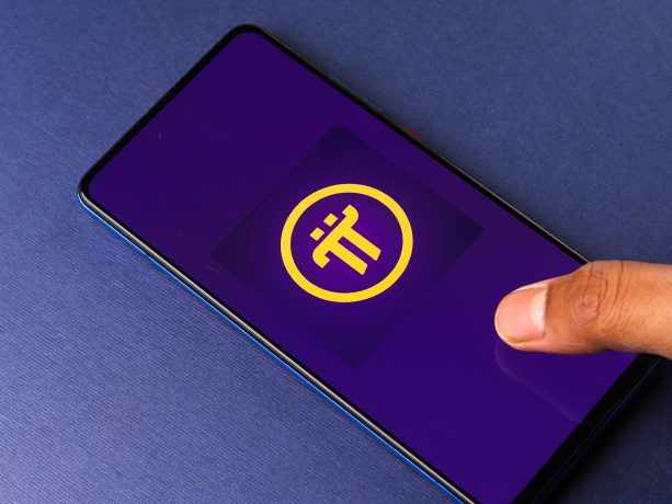 Der Finger einer Person berührt ein Smartphone, auf dem das Logo der Kryptowährung Pi Network auf einem leuchtend lila Hintergrund zu sehen ist.