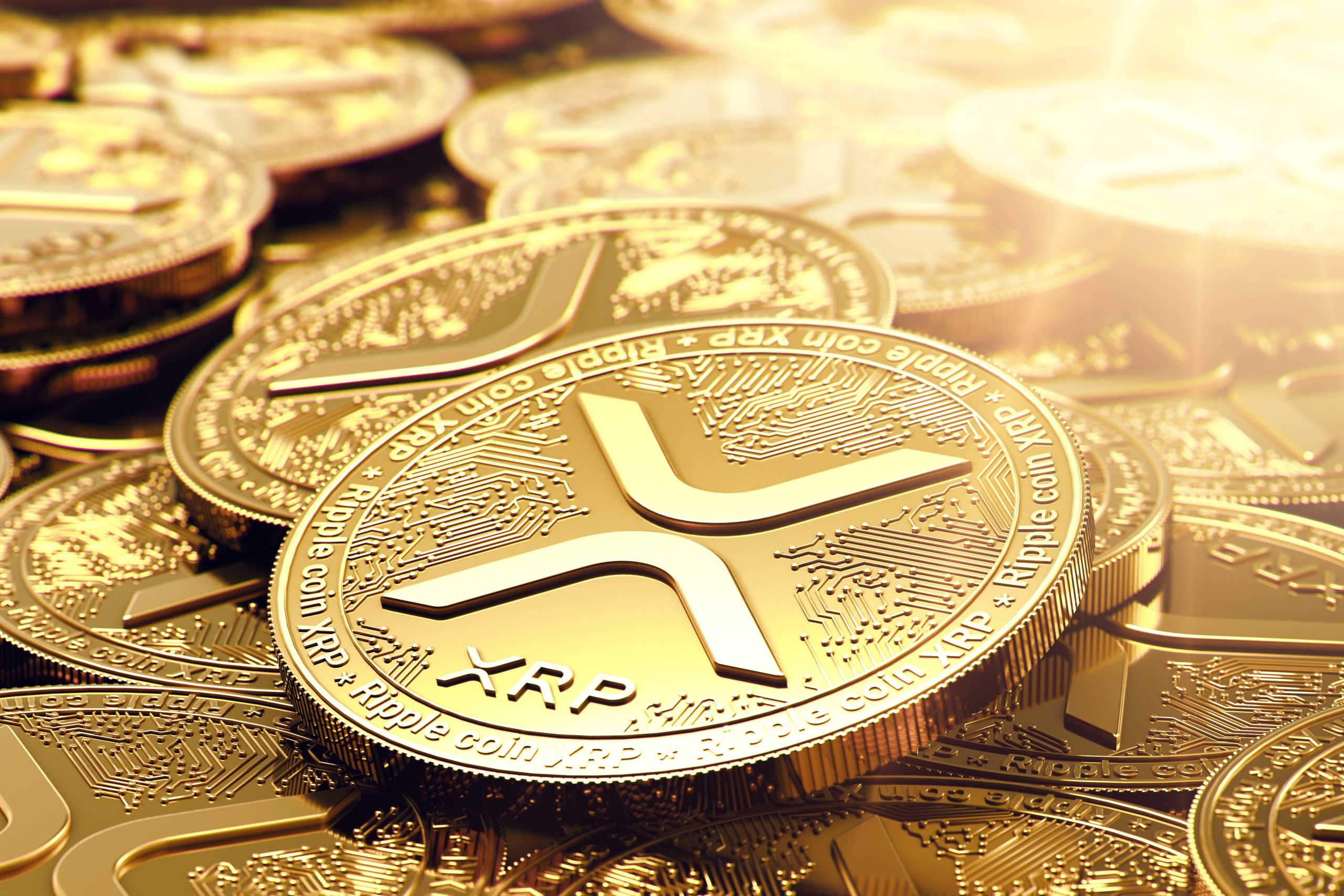 Eine Nahaufnahme mehrerer goldfarbener XRP-Kryptowährungsmünzen mit dem Ripple-Logo und kreisförmigen Mustern auf der Oberfläche, die vom Sonnenlicht beleuchtet werden - eine Anspielung auf das laufende Gerichtsverfahren von Ripple mit der SEC.