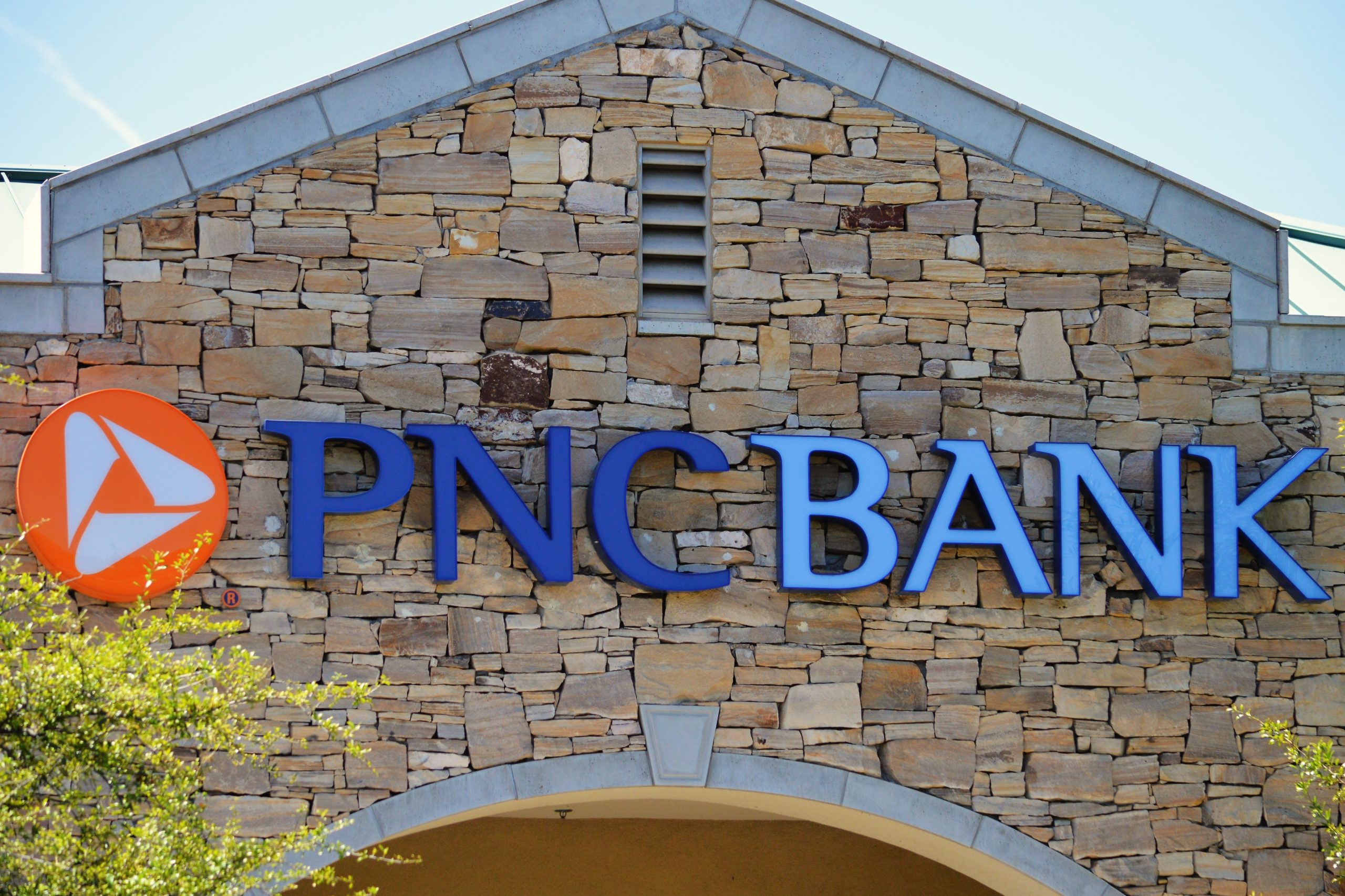 Die Vorderseite einer Filiale der PNC Bank mit dem Logo der PNC Financial Services und großen blauen Buchstaben auf einer Steinfassade.