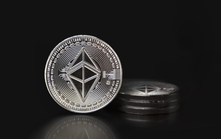Eine physische Metallmünze mit dem Ethereum-Logo steht aufrecht vor einem Stapel ähnlicher Münzen und symbolisiert die Stärke von ETH und seine Rolle in der Ethereum-Schatzkammer vor einem schlichten schwarzen Hintergrund.