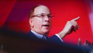 BlackRock CEO Larry Fink gestikuliert mit seiner rechten Hand, während er vor einem roten Hintergrund über die Bitcoin-ETFs von BlackRock spricht.