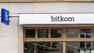 Über den Fenstern eines Gebäudes ist ein Schild mit der Aufschrift bitkom angebracht, links davon ein blaues Schild mit einem kleinen b - ein Zeichen dafür, dass sich deutsche Unternehmen auf Trends wie Bitcoin und digitale Zahlungen einstellen.