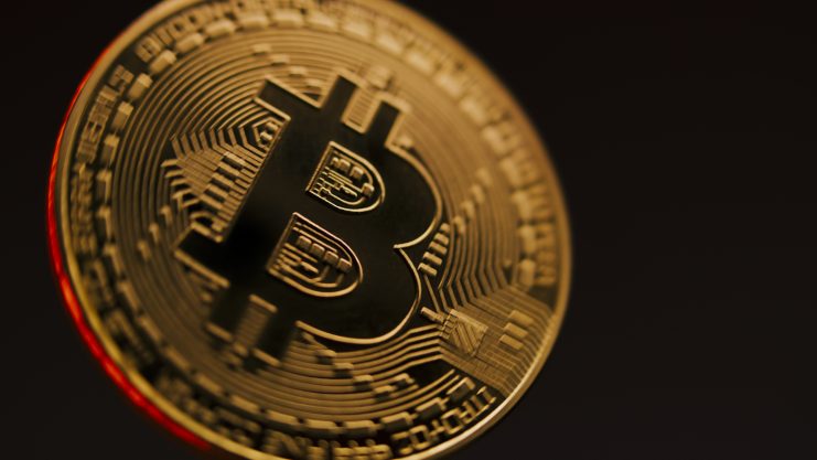 Nahaufnahme einer physischen Bitcoin-Münze in den Farben Gold und Schwarz vor einem dunklen Hintergrund.