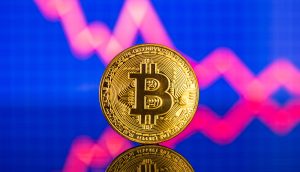 Eine goldene Bitcoin-Münze steht aufrecht mit einer abwärts gerichteten roten Kurve auf blauem Hintergrund, die einen Rückgang des Bitcoin-Wertes verdeutlicht.