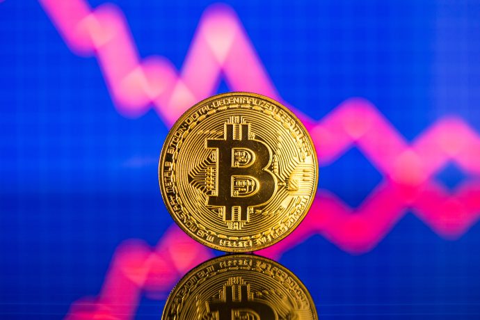Eine goldene Bitcoin-Münze steht aufrecht mit einer abwärts gerichteten roten Kurve auf blauem Hintergrund, die einen Rückgang des Bitcoin-Wertes verdeutlicht.