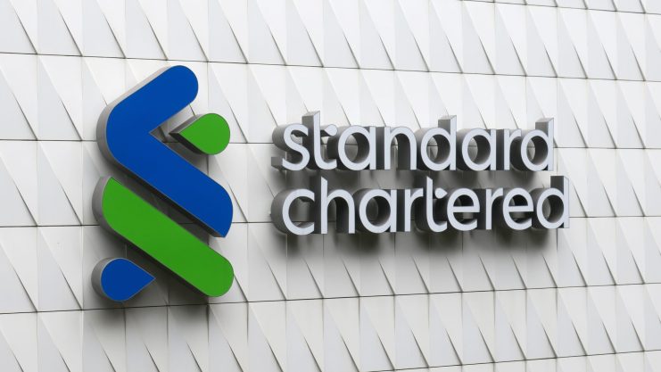 Das Logo und der Name von Standard Chartered sind auf der Außenwand des Gebäudes, die ein auffälliges weißes geometrisches Muster aufweist, gut sichtbar angebracht.