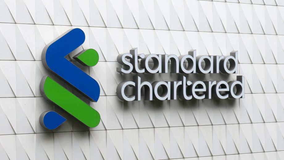 Das Logo und der Name von Standard Chartered sind auf der Außenwand des Gebäudes, die ein auffälliges weißes geometrisches Muster aufweist, gut sichtbar angebracht.