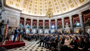 Ein Redner spricht vor einem sitzenden Publikum in einem großen Saal mit Kuppel, Kronleuchtern, Statuen und amerikanischen Flaggen über die Krypto-Gesetze vor dem US-Kongress.