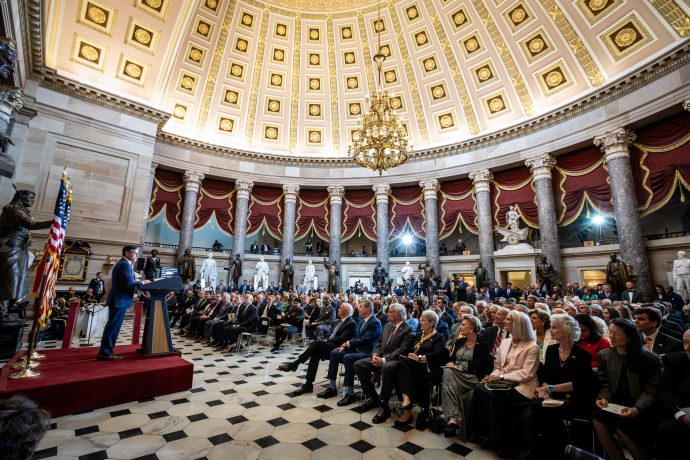 Ein Redner spricht vor einem sitzenden Publikum in einem großen Saal mit Kuppel, Kronleuchtern, Statuen und amerikanischen Flaggen über die Krypto-Gesetze vor dem US-Kongress.
