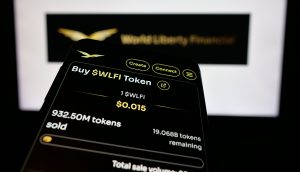 Ein Smartphone-Bildschirm zeigt die Option zum Kauf von WLFI-Token zu je $0,015 an. Es werden 932,50 Millionen Token verkauft und 19,07 Millionen WLFI-Token verbleiben. Im Hintergrund ist das World Liberty Financial-Logo zu sehen.