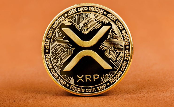 Physische goldene XRP-Münze vor orangefarbenen Hintergrund