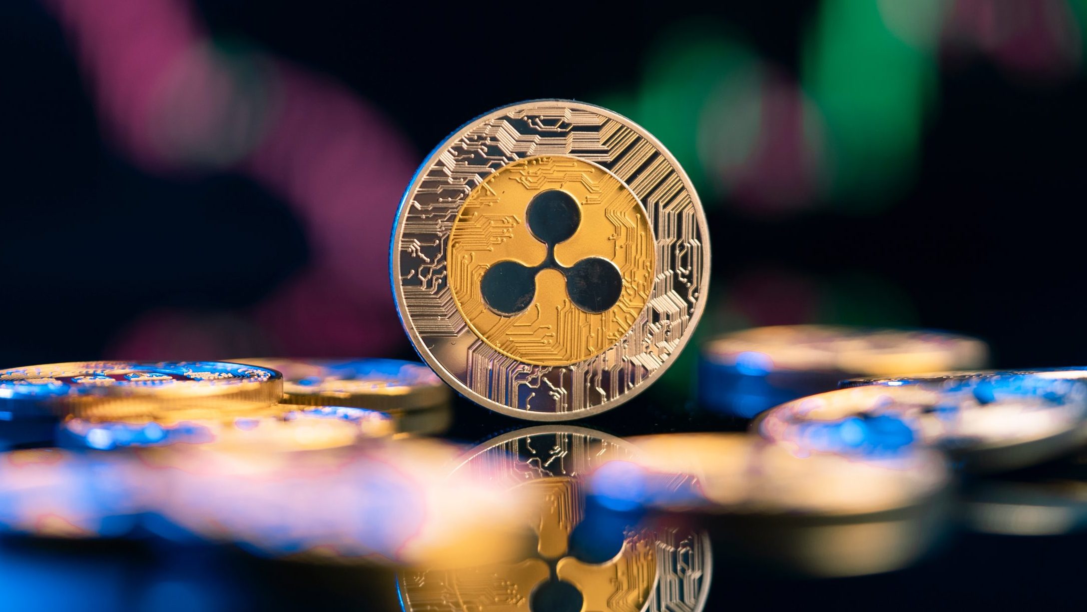 Eine XRP-Kryptowährungsmünze steht aufrecht zwischen anderen Münzen, mit einer unscharfen digitalen Grafik im Hintergrund.