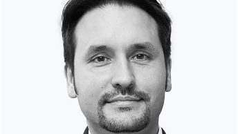 Dr. André Dragosch mit dunklem Haar und Spitzbart, der eine Anzugsjacke und ein weißes Hemd trägt, posiert vor einem schlichten hellen Hintergrund und strahlt die ruhige Zuversicht eines Bitcoin-Enthusiasten aus.
