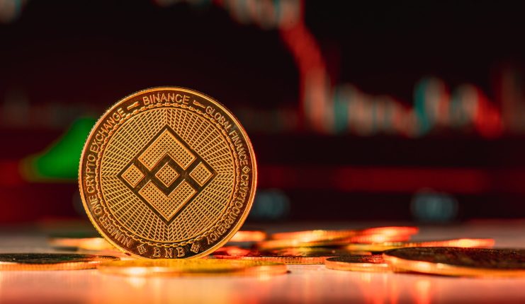 Zu sehen ist ein BNB Coin vor einem Krypto-Chart
