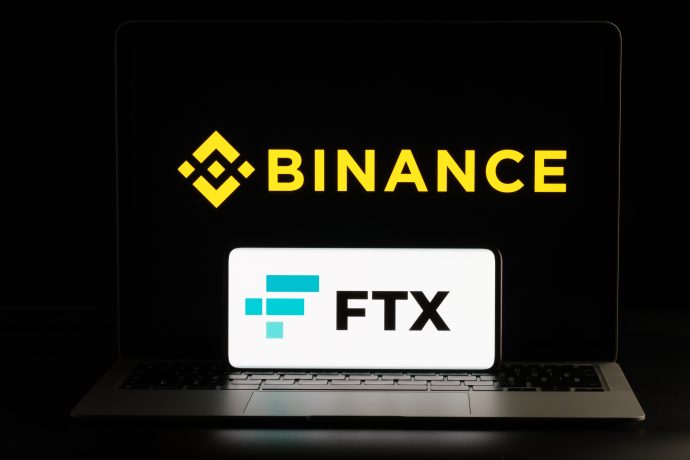 Ein Laptop zeigt das Binance-Logo auf seinem Bildschirm, ein mobiles Gerät davor das FTX-Logo.