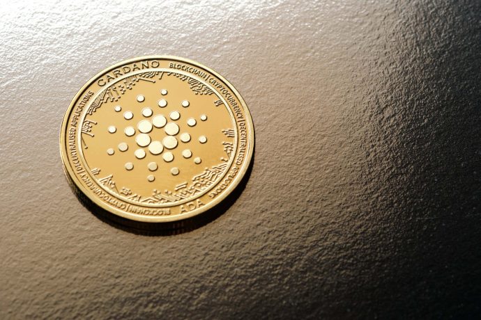 Eine goldfarbene Cardano ADA-Kryptowährungsmünze ruht auf einer strukturierten dunklen Oberfläche, die die Eleganz von Cardano unterstreicht.