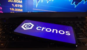 Ein Smartphone mit dem Cronos-Logo liegt auf einer Laptop-Tastatur, während auf dem Laptop-Bildschirm im Hintergrund Kursziele und Börsenzahlen erscheinen.